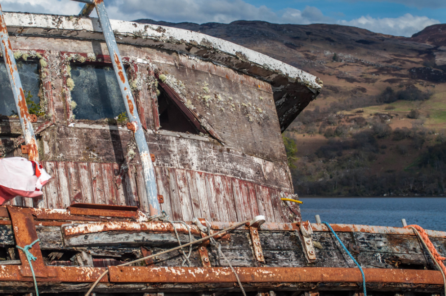 Picture of an abandonded ship covered in moss and algae with hills in the background